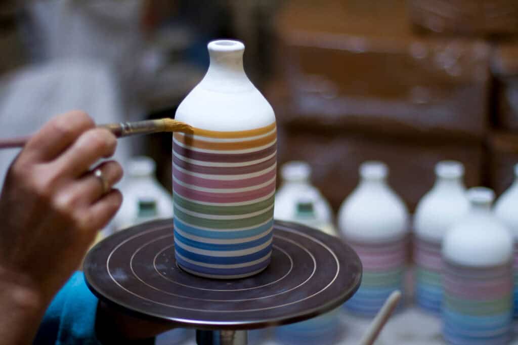Mani di un artigiano pugliese mentre dipinge a mano un orcio in ceramica della collezione Arcobaleno per Frantoio Muraglia.